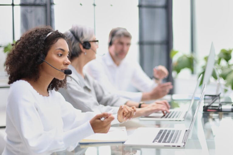 Drei Personen mit Headsets, konzentriert arbeitend an Laptops in einem modernen Büro.