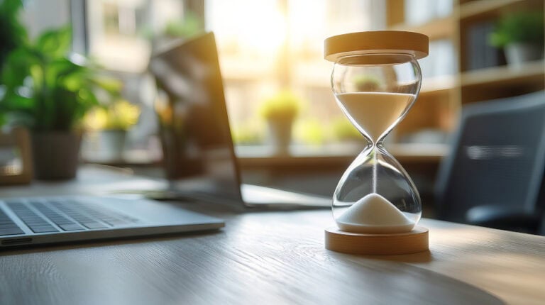 Schreibtisch mit Laptop und Sanduhr als Symbol für Zeitarbeit